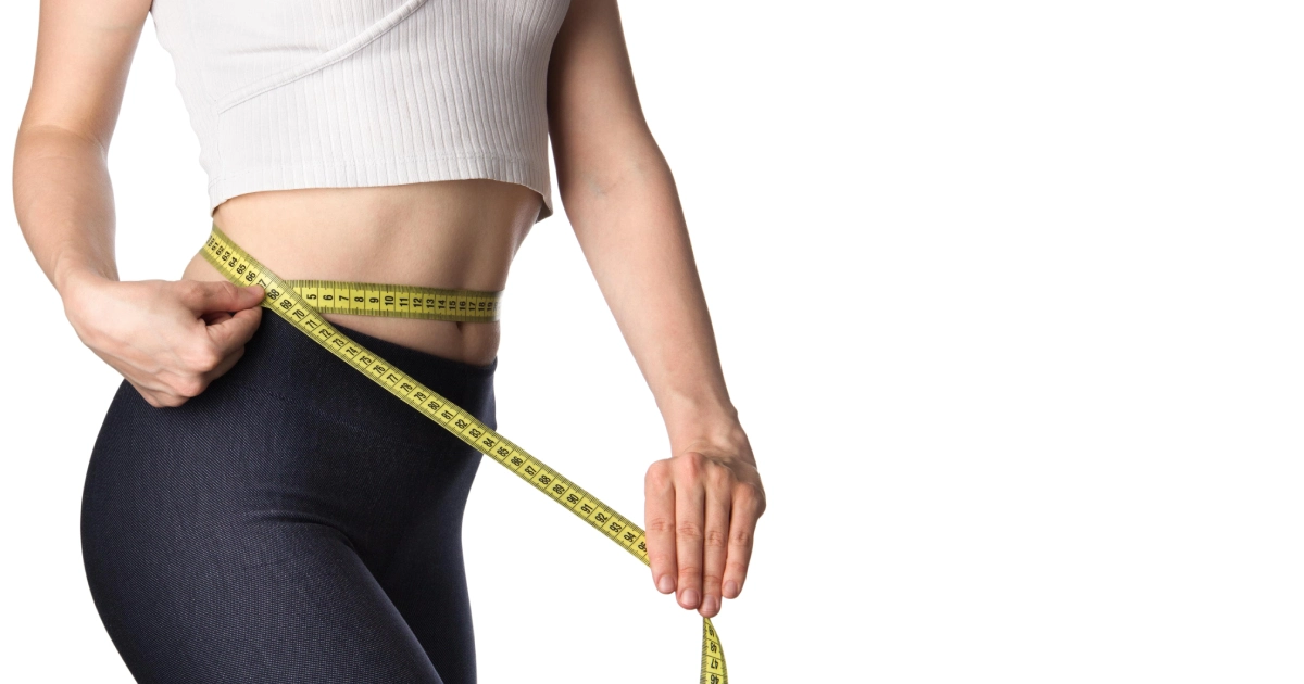 A woman in workout clothes measuring her waist with a yellow tape measure during Weight Loss in Great Neck, NY.